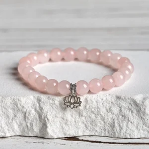 Pink crystal lotus charm bracelet with 925 sterling silver pendant displayed on stone with overhead view