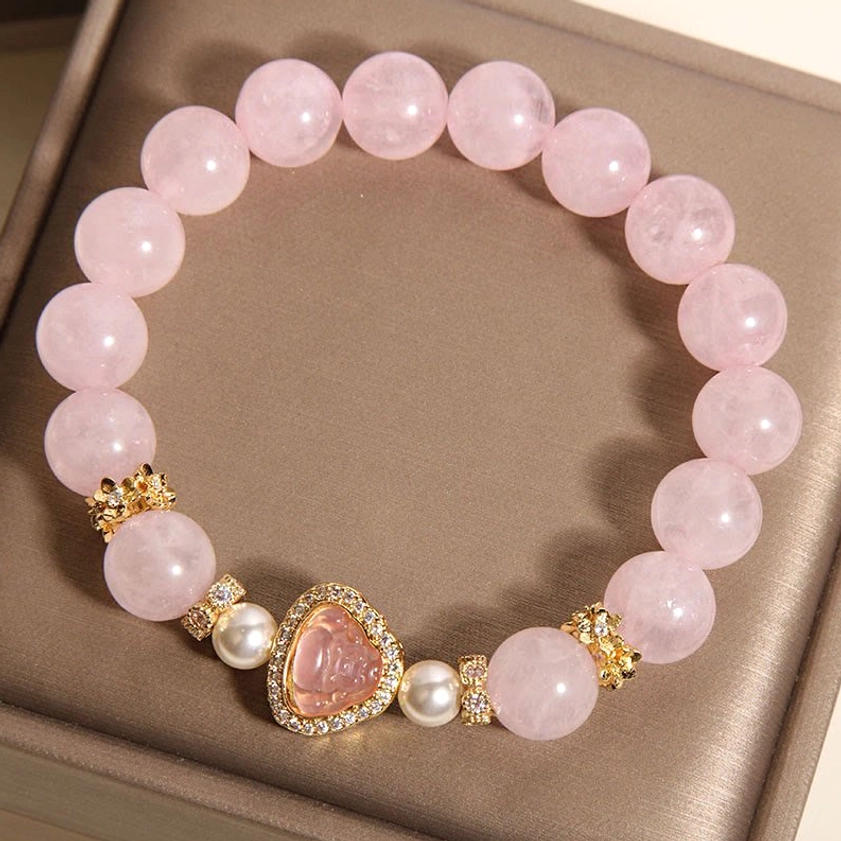 Pink crystal pearl Buddha bracelet high side overhead view on brown jewelry tray featuring smooth round pink quartz beads with gold-toned Buddha charm and spacers