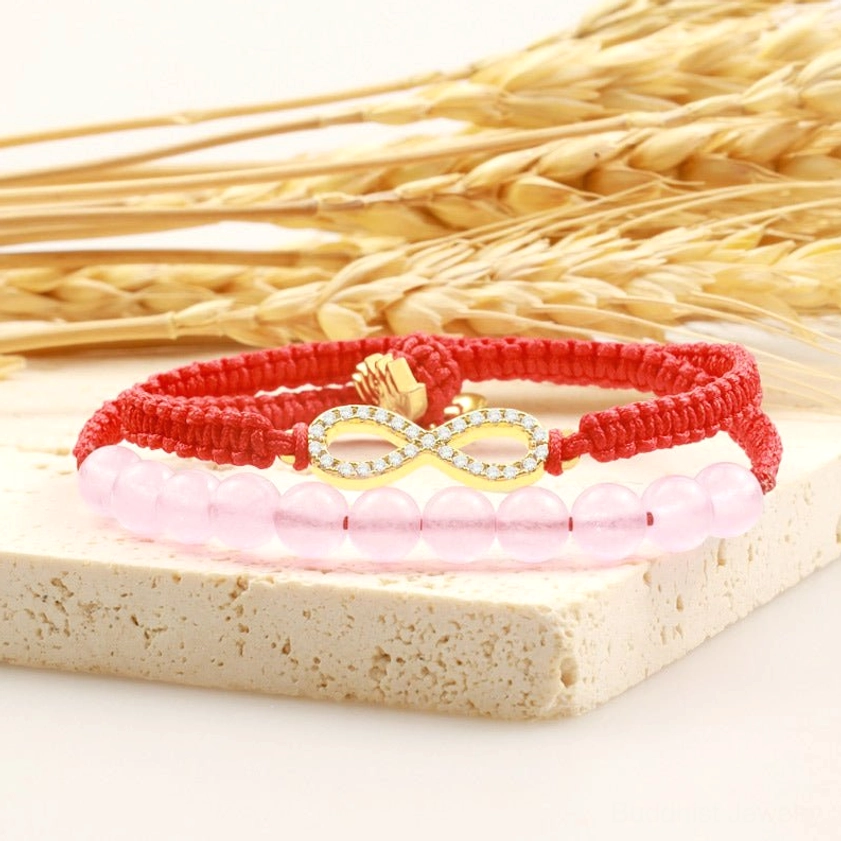 Dual-layer Buddhist red string bracelet with pink crystal beads and gold lotus clasp low angle view on stone background