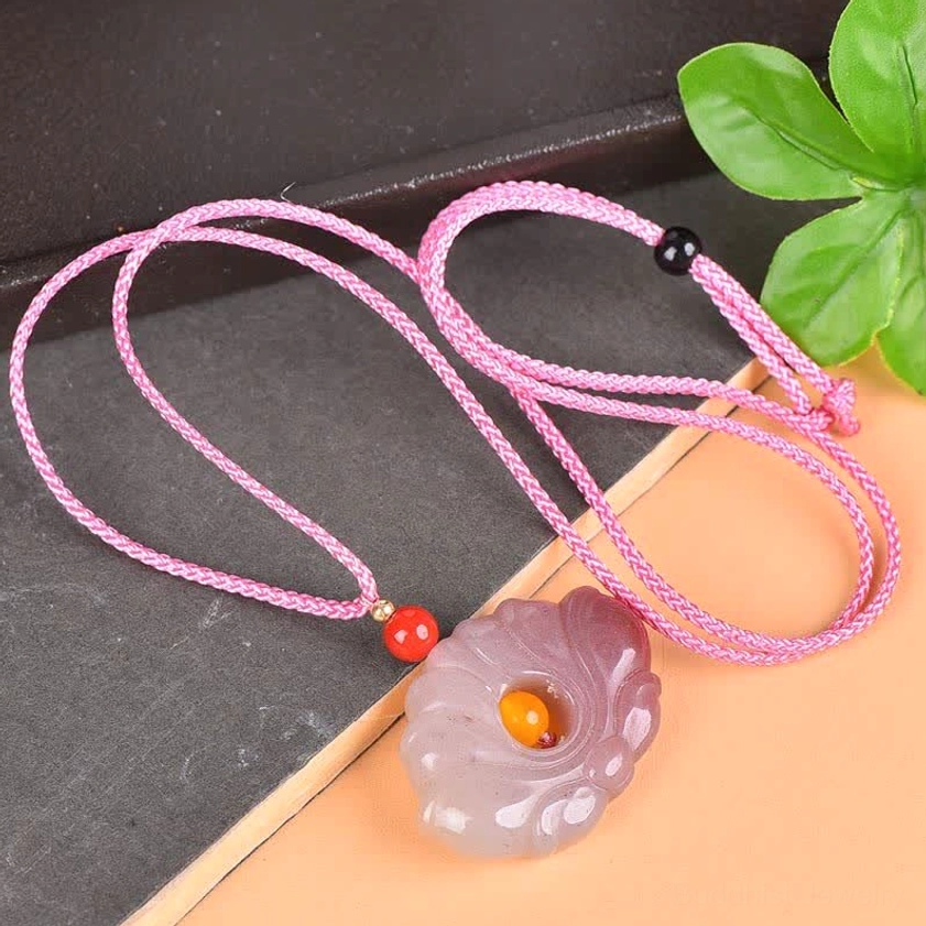 Buddhist lotus jade pendant necklace flat lay with pink braided cord and green foliage