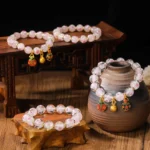 Luminous pink heart fluorescent liuli glass Buddhist blessing bracelet with gold charms displayed in multi-angle overhead view on traditional wooden furniture