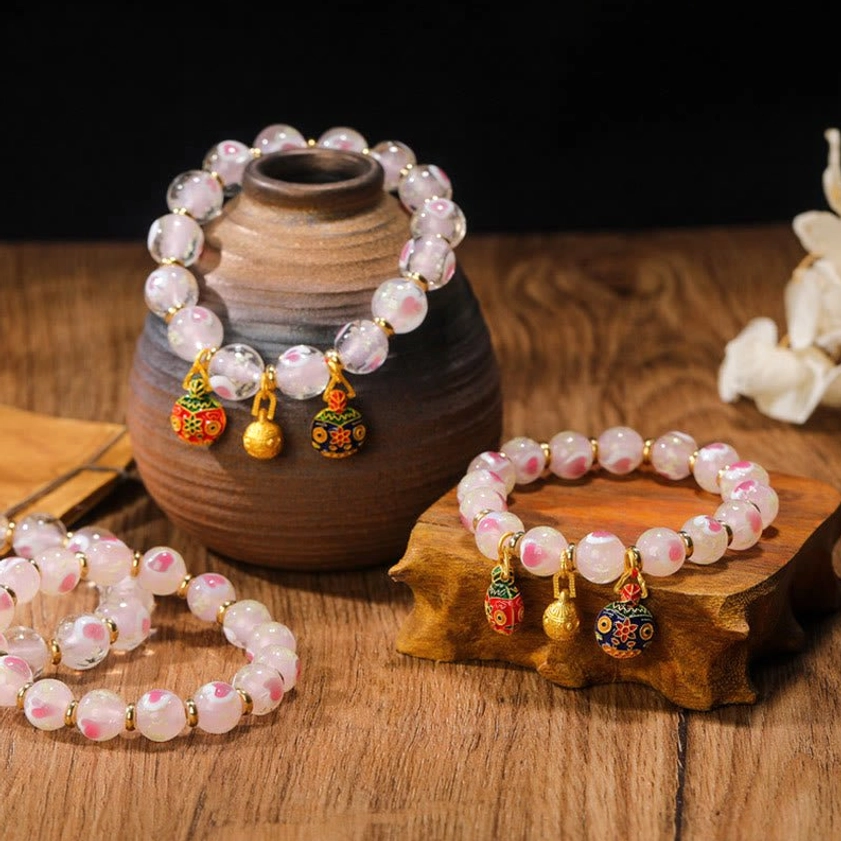 Set of matching pink luminous heart Buddhist blessing bracelets in multiple styles displayed overhead with enamel pendants and gold spacers on vintage wooden desktop