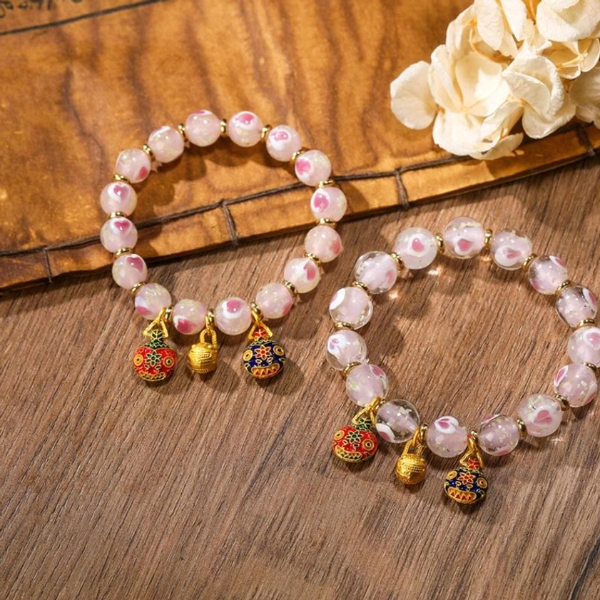 Pair of pink luminous heart Buddhist blessing bracelets arranged flat lay with enamel metal charms and gold accessories on vintage wooden table