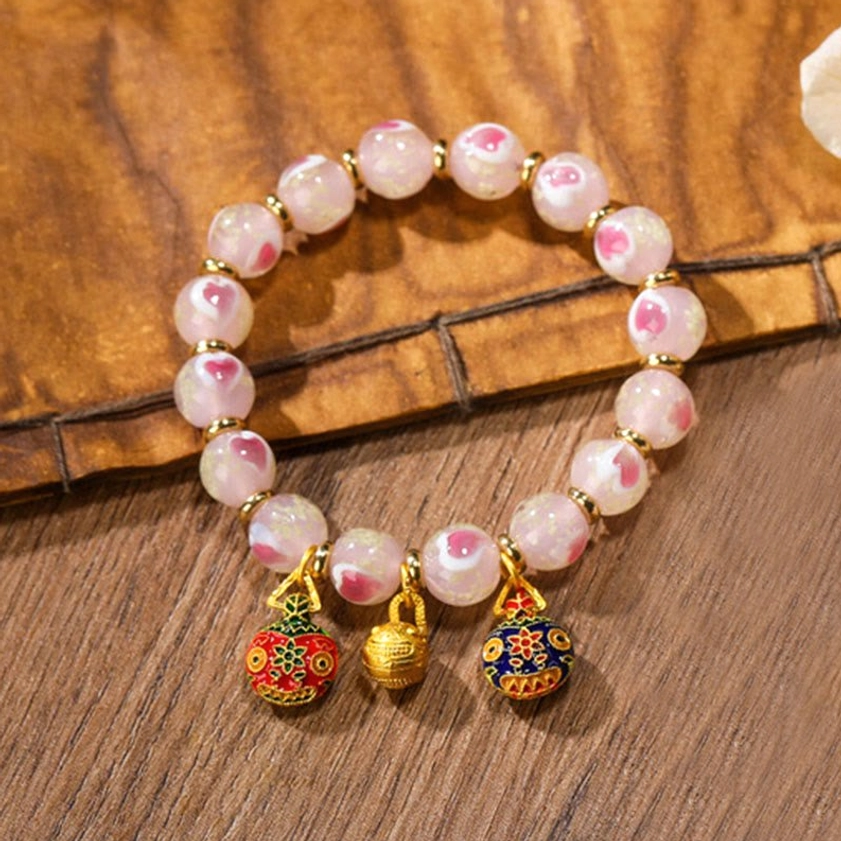 Close-up oblique view of single pink luminous heart Buddhist bracelet with enamel metal pendants and gold spacer beads on wooden table with bamboo cushion