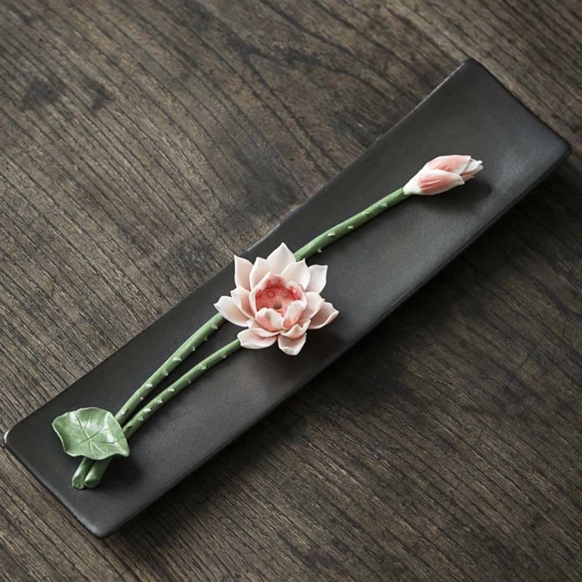 Pink lotus ceramic incense holder with green foliage on matte black tray, flat overhead view