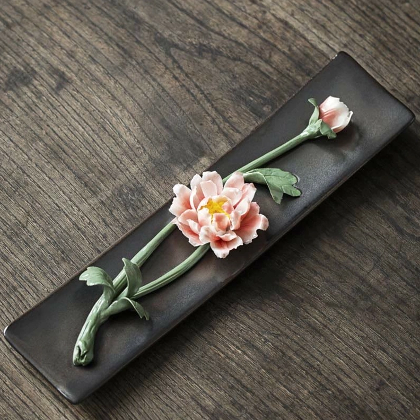 Single pink peony ceramic incense holder with green stem detail, flat lay perspective on dark wood surface