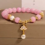 Pink Quartzite Lotus Pearl Buddhist Bracelet - Overhead oblique view displaying 8mm pink quartzite beads, freshwater pearl, and gold-toned lotus charm pendant on wooden display