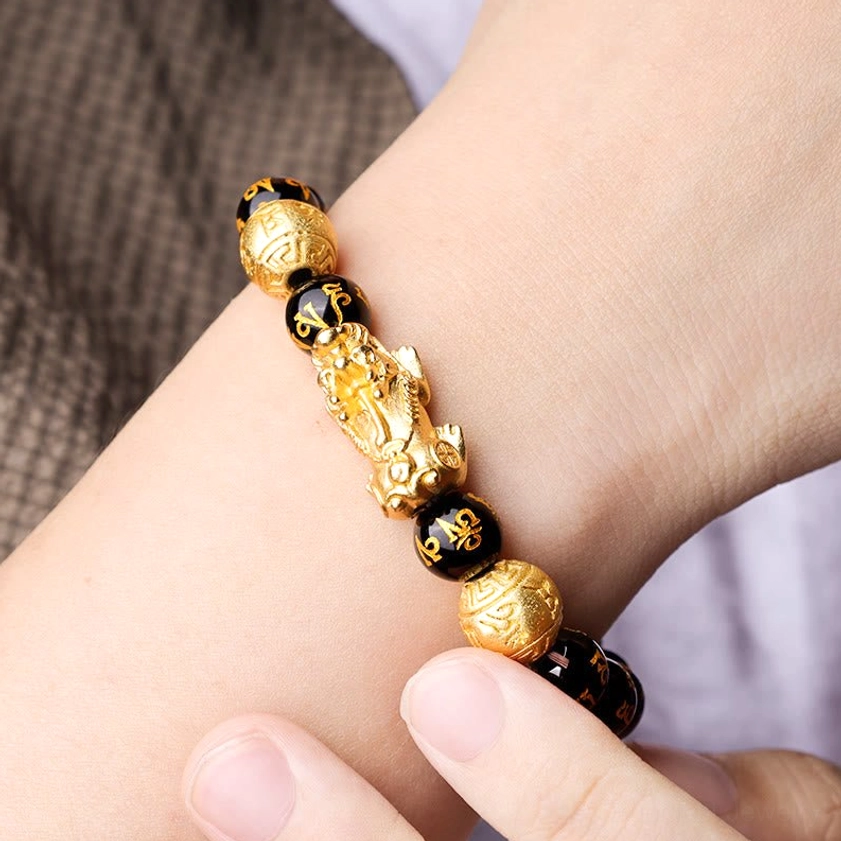 Woman wearing black obsidian Pixiu bracelet with gold mantra inscriptions and golden prosperity charm on wrist