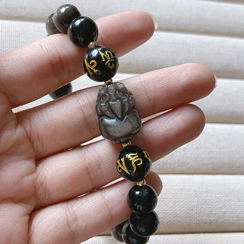 Detail shot of Pixiu charm and black obsidian beads on protective Buddhist bracelet held by fingers