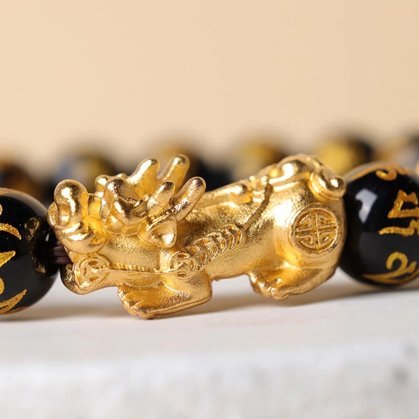 Close-up detail of golden Pixiu charm with intricate sculpture and black obsidian beads engraved with Om Mani Padme Hum mantra
