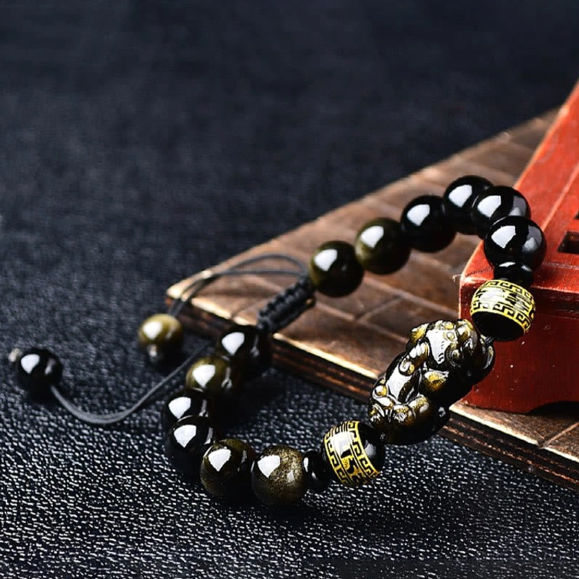 Close-up 3/4 angle view of gold sheen obsidian Pixiu charm and engraved spacer beads on braided cord