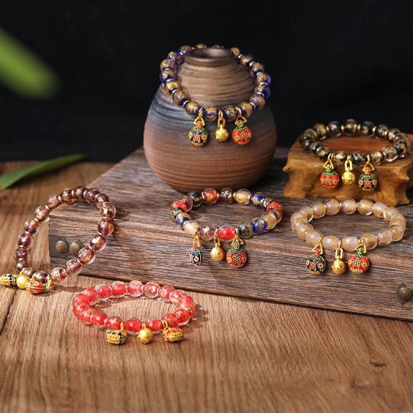 Assorted Buddhist blessing bracelets with Pixiu family charms and gold bells arranged on ceramic pot - handmade Liuli glass beads fortune protection bracelet
