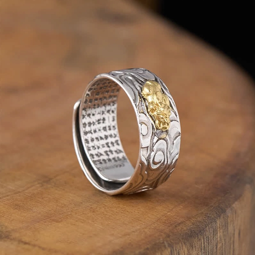 Pixiu Heart Sutra Buddhist ring 3/4 side view showing bicolor design with inner sutra engraving, warm wooden table setting