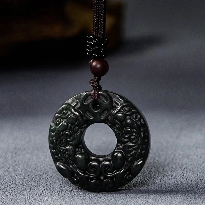 Handcrafted black-green jade Pixiu pendant with intricate carving and wooden bead accent on grey fabric background