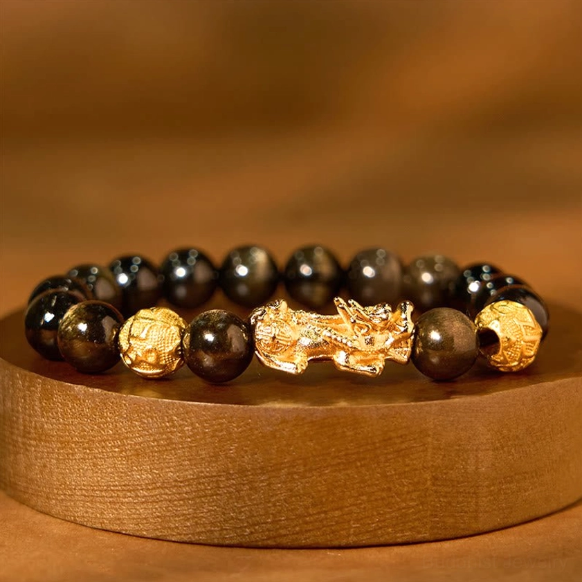 Gold sheen obsidian Pixiu wealth bracelet flat lay on wooden round display stand, featuring dark brown-black obsidian beads with gilded Pixiu and carved gold accent beads