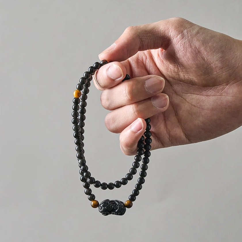 Pixiu obsidian wealth bracelet held in hand showing carved charm obsidian beads and protective crystal composition