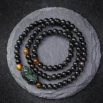 Pixiu obsidian wealth bracelet with rainbow and black obsidian beads, hand-carved Pixiu charm, overhead view on slate background