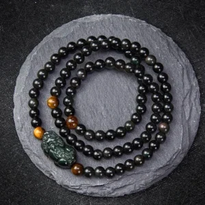 Pixiu obsidian wealth bracelet with rainbow and black obsidian beads, hand-carved Pixiu charm, overhead view on slate background