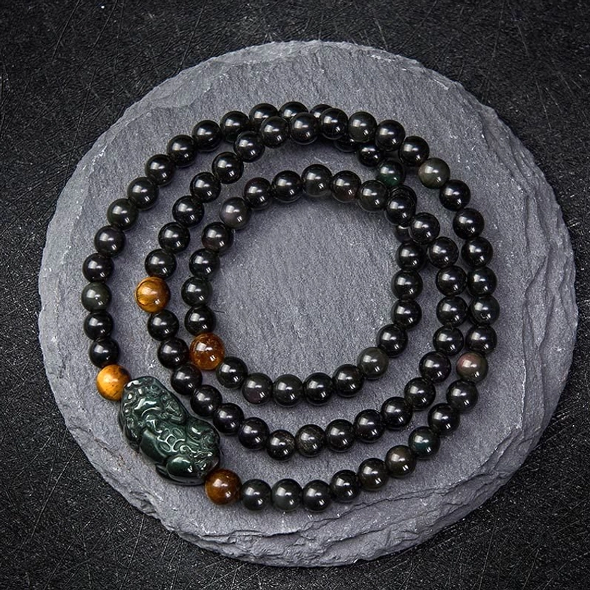 Pixiu obsidian wealth bracelet with rainbow and black obsidian beads, hand-carved Pixiu charm, overhead view on slate background