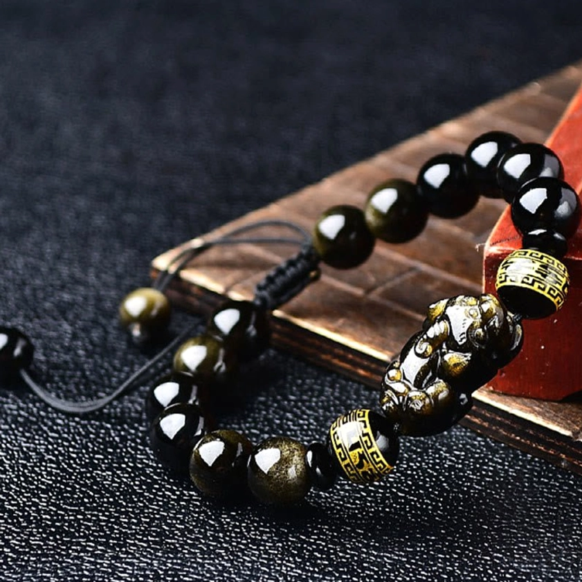 Close-up side view of handmade Pixiu charm and polished obsidian beads with braided black cord and adjustable knot