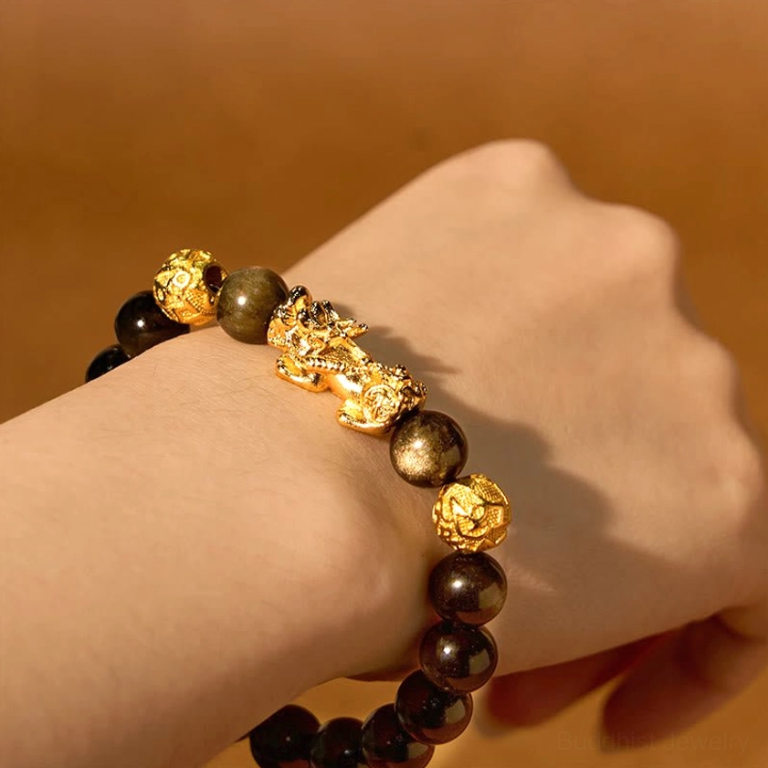 Pixiu wealth bracelet worn on side of hand and wrist against warm brown background, clearly showing the gilded Pixiu charm and protective design