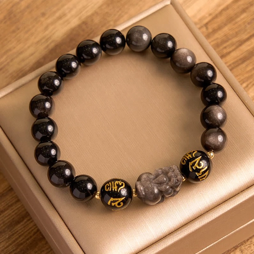 Handmade Buddhist protection bracelet featuring silver sheen obsidian and Pixiu charm displayed on wooden jewelry tray
