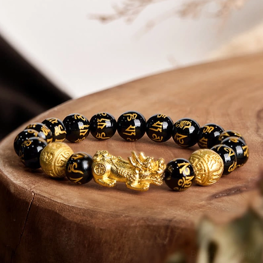 Black obsidian Pixiu wealth bracelet with golden charm on wooden display stand, overhead view showing engraved beads and spacers