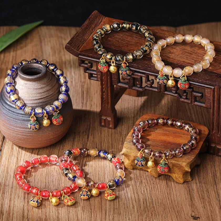 Collection of handmade Pixiu prosperity bracelets with gold-plated charms and assorted Liuli glass beads displayed on wooden table - Buddhist fortune bracelet multiple styles