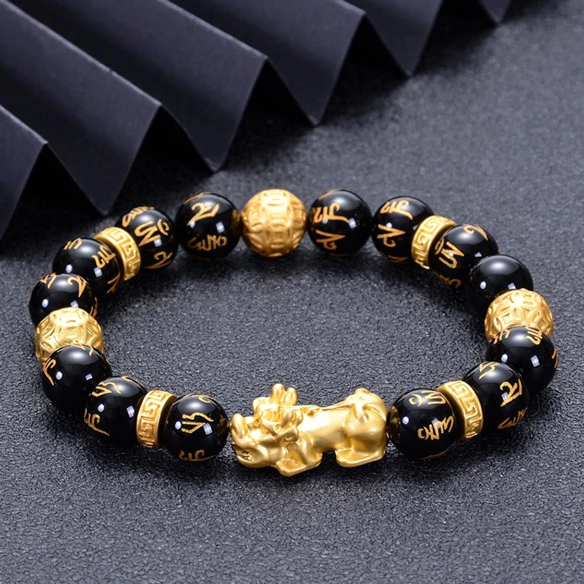 Pi Xiu strength bracelet featuring smooth black obsidian beads and golden protective charms on fabric background
