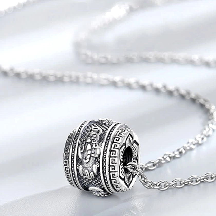 Cylindrical rotating Pixiu pendant close-up showing vintage silver texture, hollow side design with embossed Buddhist motifs