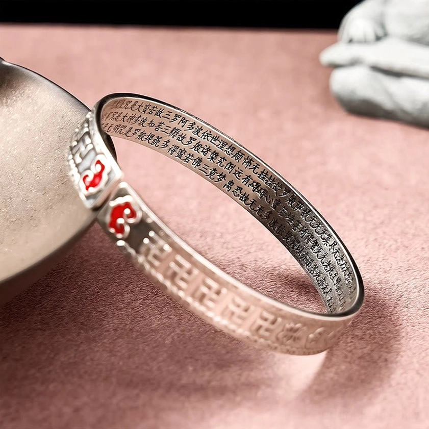 Pixiu silver bangle bracelet close-up showing engraved Buddhist text and red enamel details with stone background