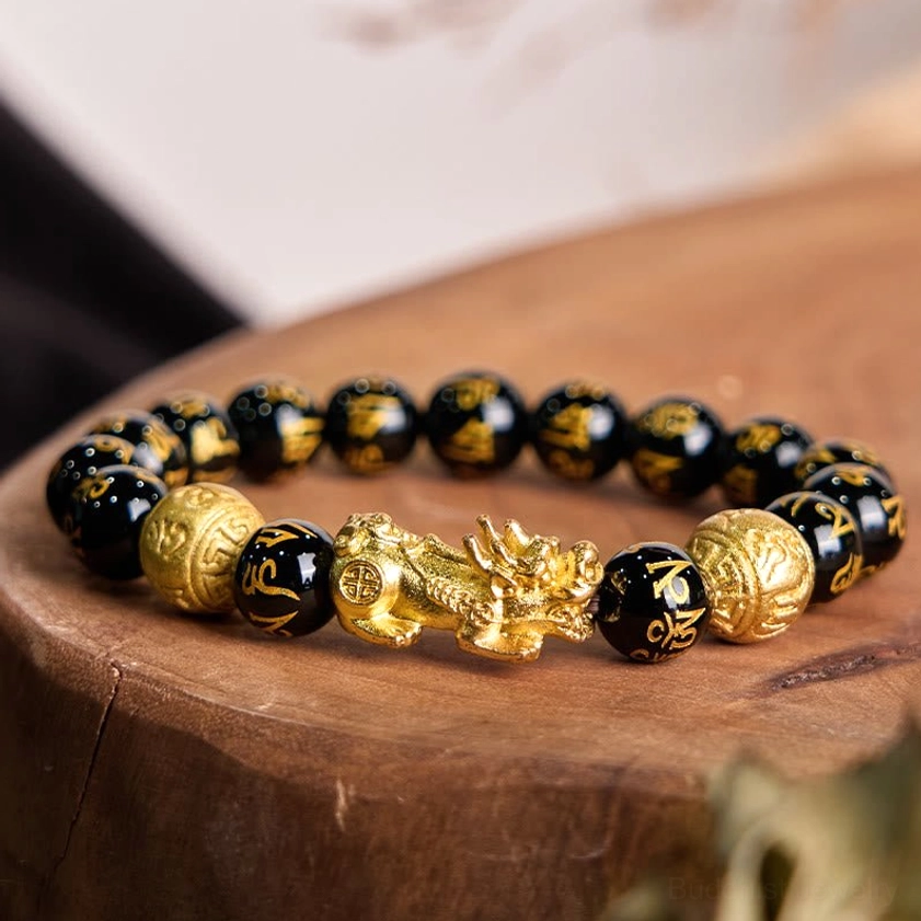 Top view of black obsidian Pixiu bracelet displaying golden Pixiu charm, engraved beads, and gold spacer details on wooden table
