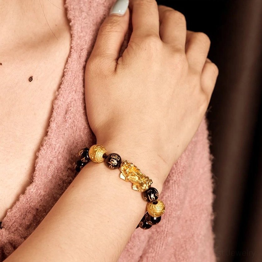 Woman wearing black obsidian Pixiu wealth bracelet on left wrist, close-up side view showing bracelet worn on skin with soft fabric background
