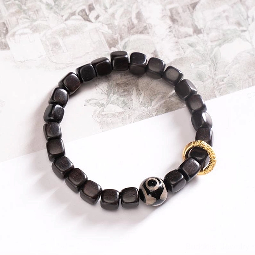 Plain ebony wood cubic bead bracelet with gold-toned metal ring on printed paper background, meditation bracelet style