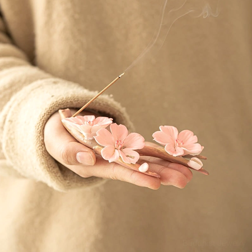 Handheld ceramic plum blossom incense holder held in palm, beige knit sleeve visible, eye-level close-up