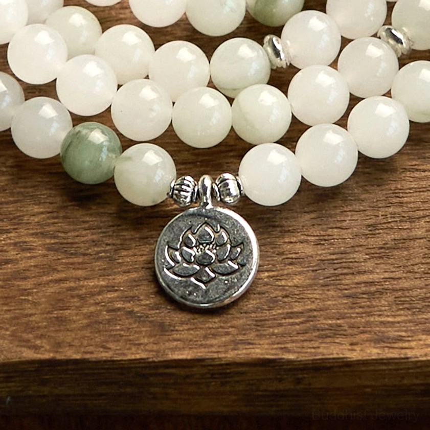 Polished jade mala beads bracelet on wooden table, featuring green accent beads and detailed silver lotus charm