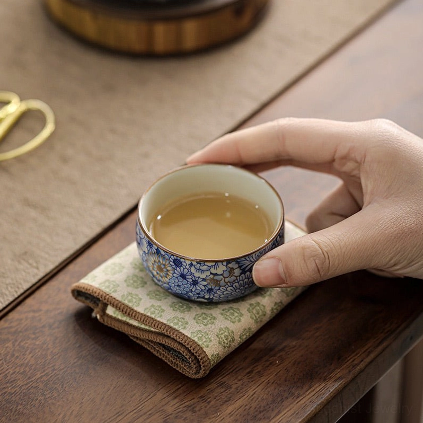 Handcrafted porcelain teacup filled with light yellow tea held by hand on wooden tea table