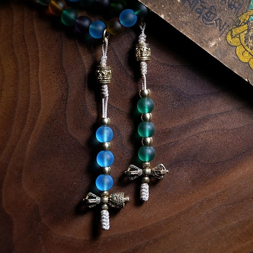 Pair of Tibetan prayer bead counters in silver-toned metal with matching glass bead tassels, vintage script card backdrop, overhead shot