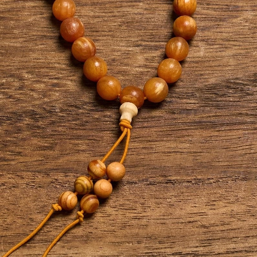 Detailed side view of large smooth resin-rich pine wood beads and guru bead with tassel on wood table
