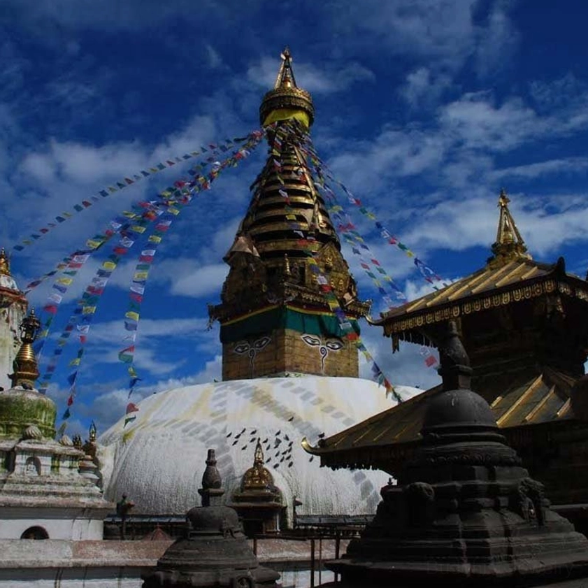 Long string of Buddhist prayer flags stretched between ancient stupas in traditional spiritual complex under cloudy sky