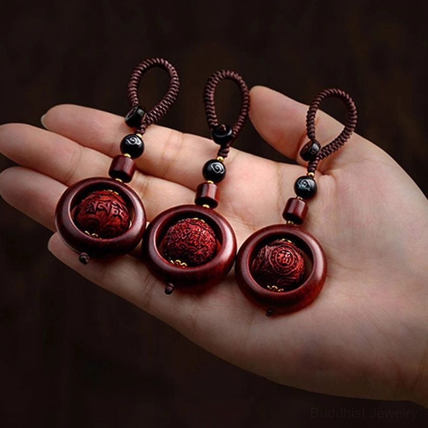 Three matching red sandalwood prayer keychain pendants held in human palm showing carved details and matching decorative beads
