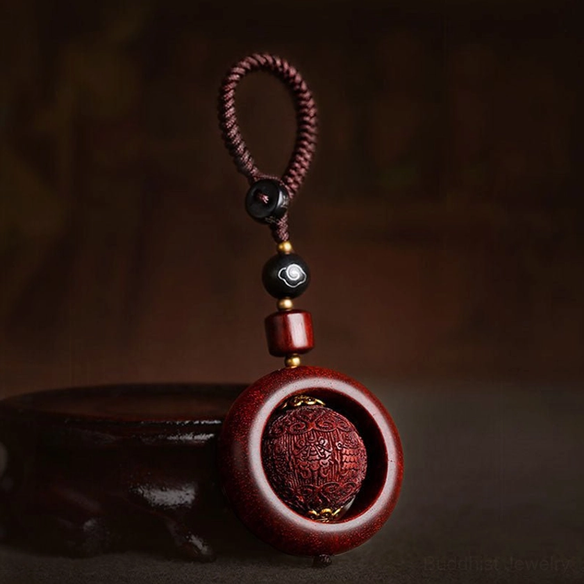 Red sandalwood rotating prayer keychain side view with rotatable carved wooden sphere and braided lanyard on dark display background
