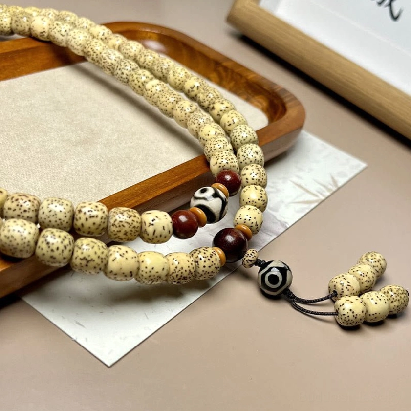 Buddhist prayer beads side flat lay showing draped Bodhi seed mala with matching Dzi bead charm on paper surface
