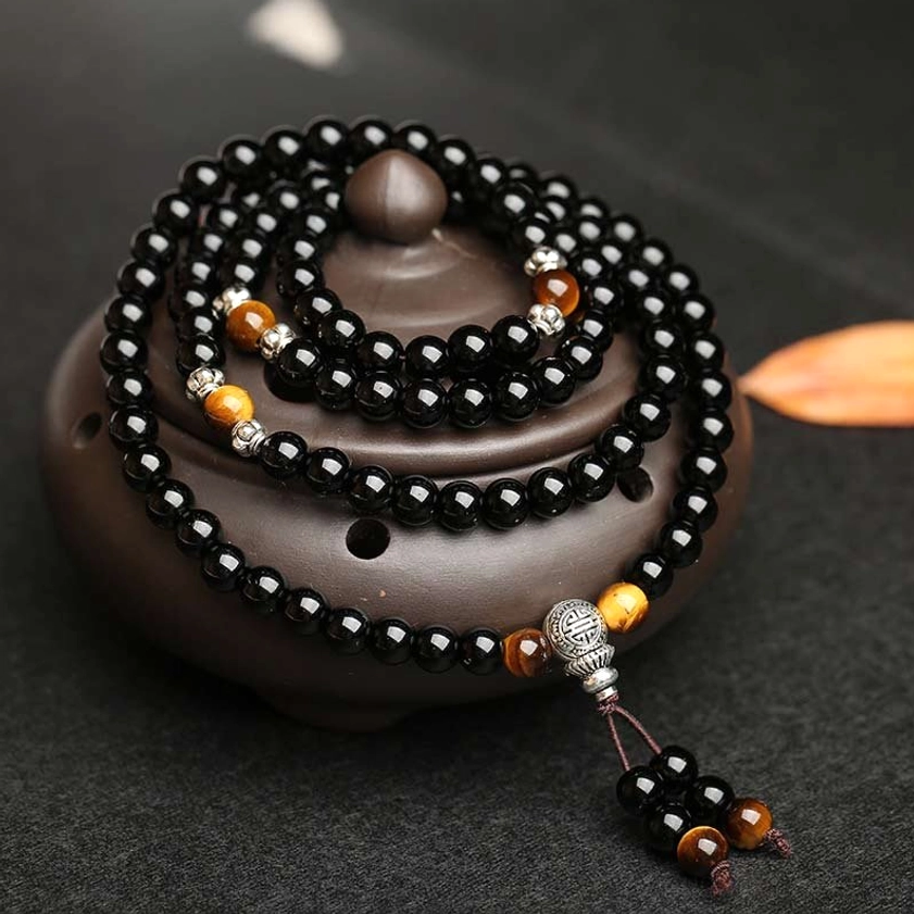 Coiled Buddhist prayer mala with black obsidian, tiger eye accents, and silver tassel pendant, overhead shot