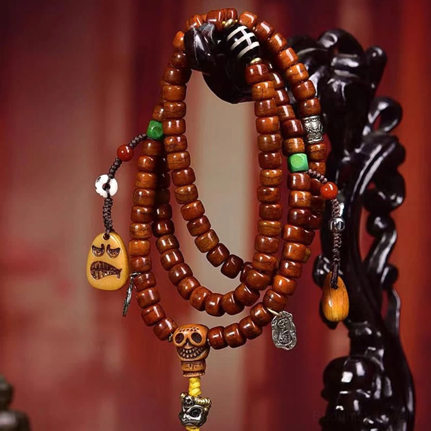 Hanging Buddhist 108-bead mala bracelet showing intricate bone beads, skull guru charm, grimace pendant and metal decorations on black wood stand