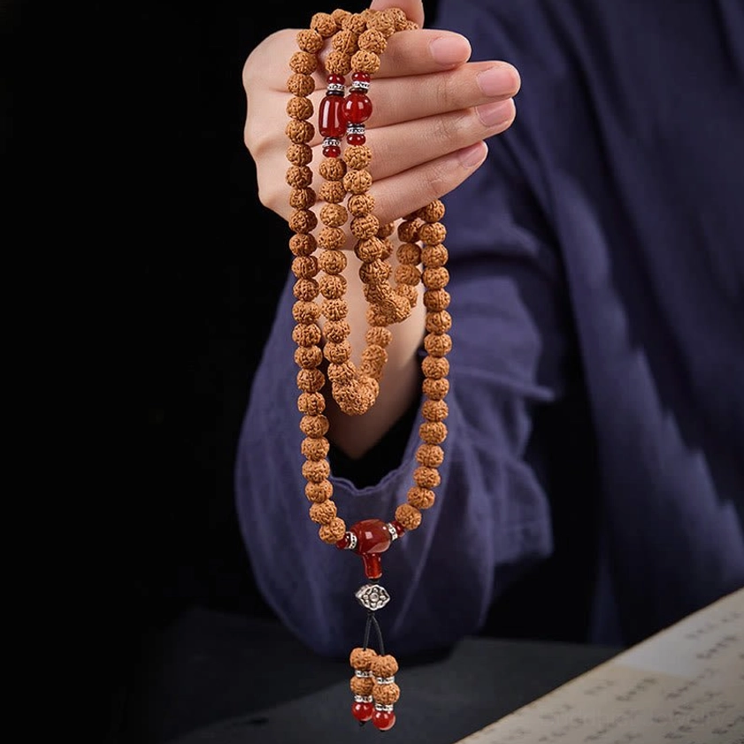Hand holding Buddhist prayer mala beads showing texture and craftsmanship of bodhi seeds and metal hardware