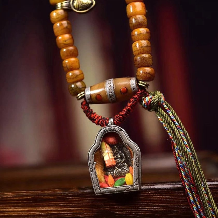 Authentic Buddhist prayer mala three-quarter eye-level view showing aged camel bone beads, silver-inlaid dzi stone, woven multicolor protective tassel, and spiritual symbolism