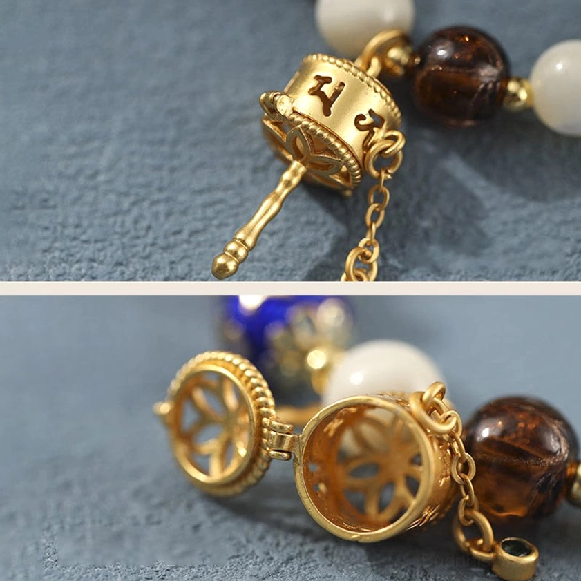Gilt metal prayer wheel charm close-up with engraved Om mantra, hollowed design and detailed bead chain