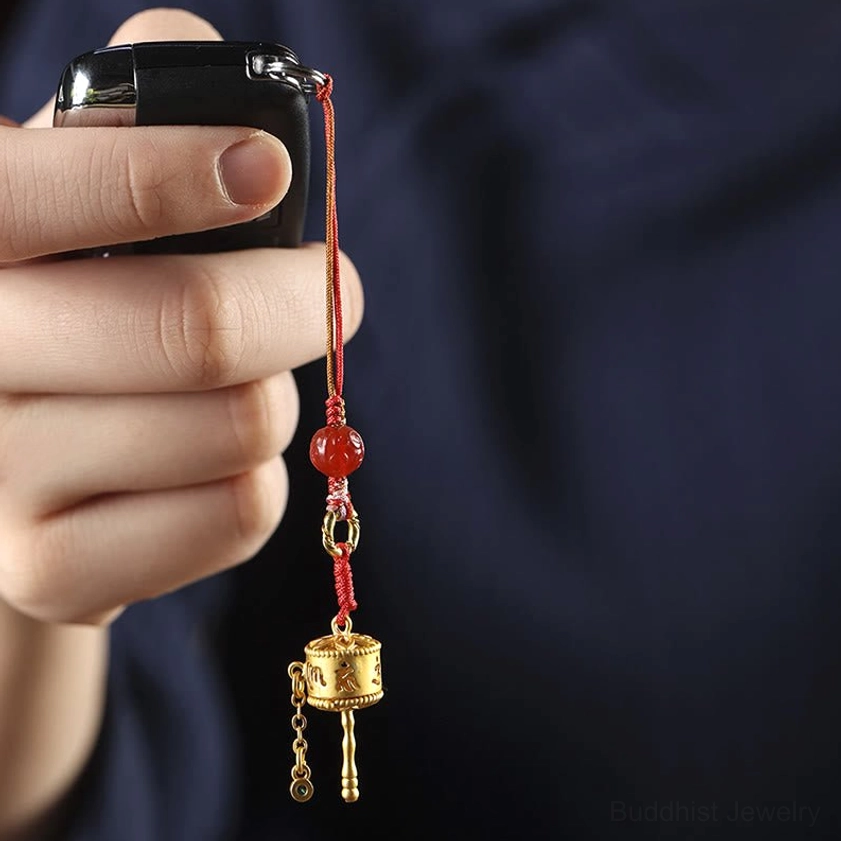 Hand-held Om Mani Padme Hum prayer wheel charm attached to electronic device showing solid red braided cord