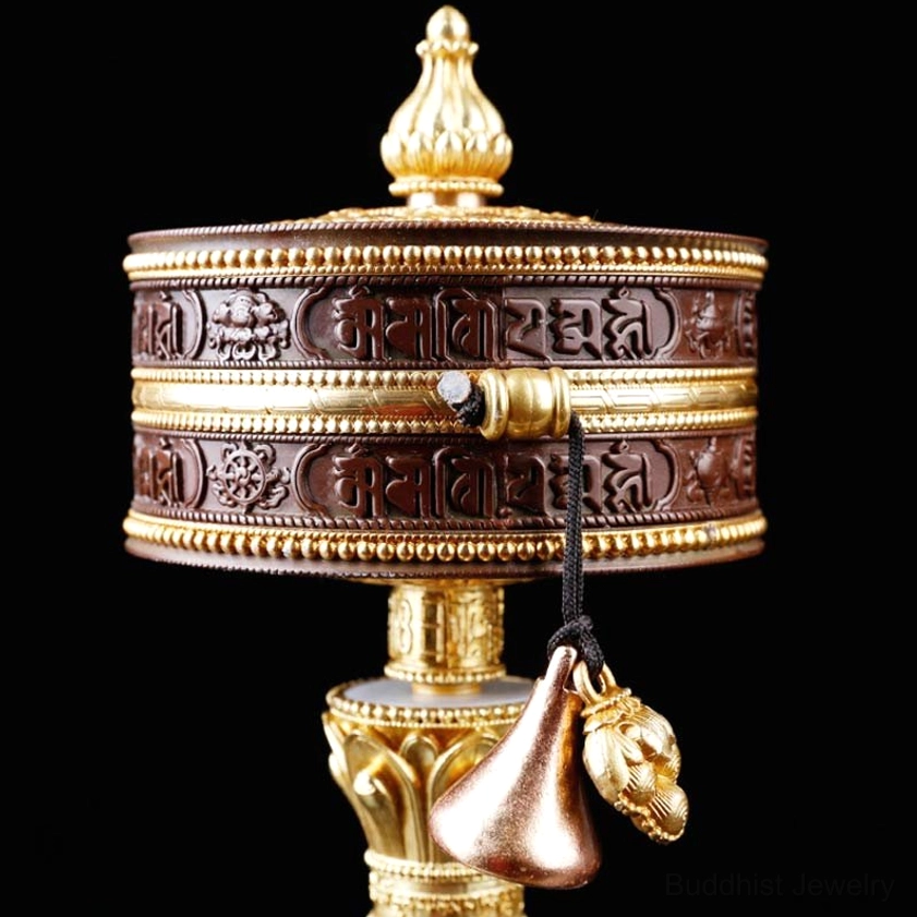 Close-up of prayer wheel assembly with embossed Sanskrit scriptures, gold metal accents, and decorative lion-head bell